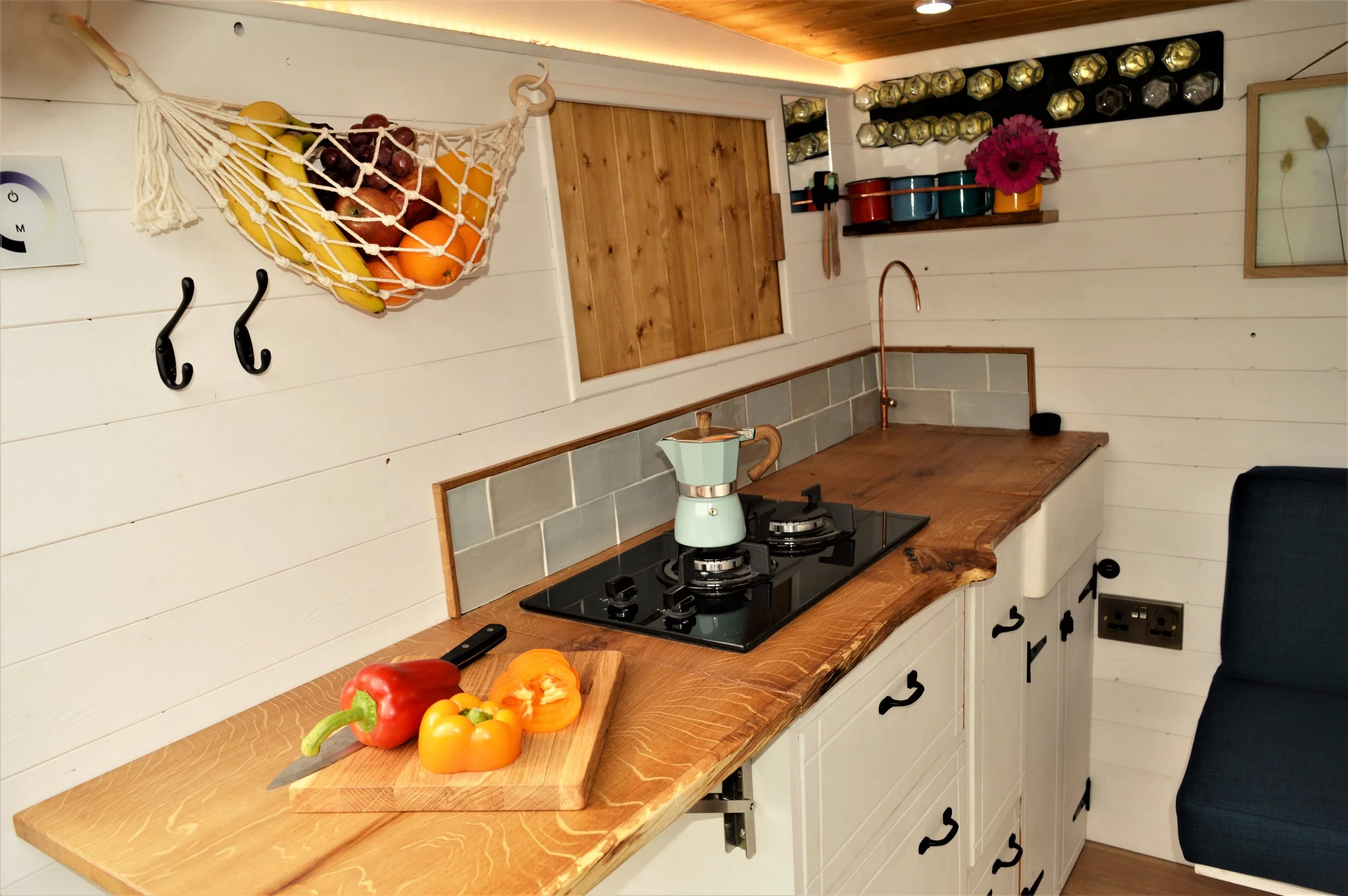 A campervan kitchen with a timber worktop, copper tap, and handmade details.