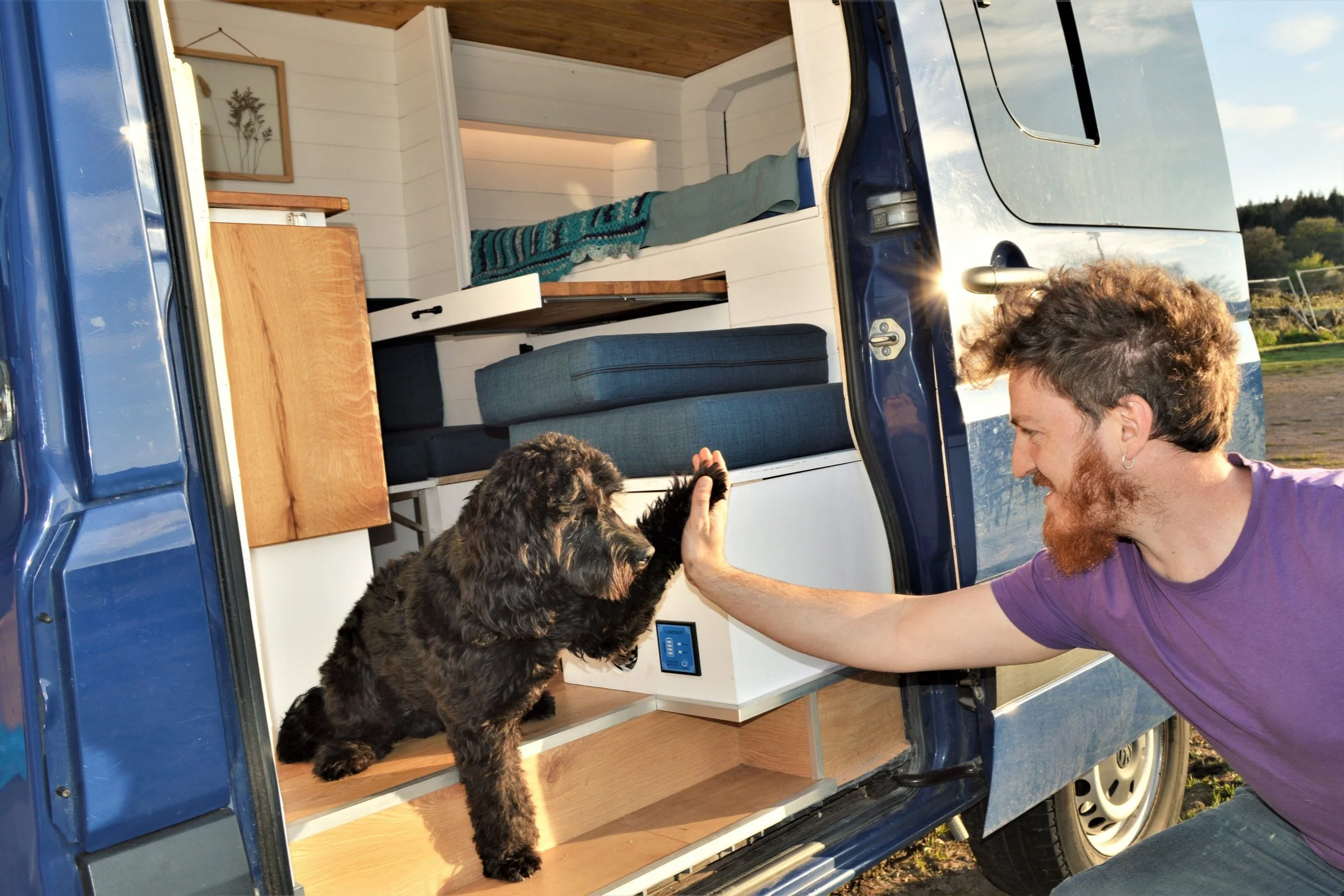 A person and a dog at the open door of a converted van.