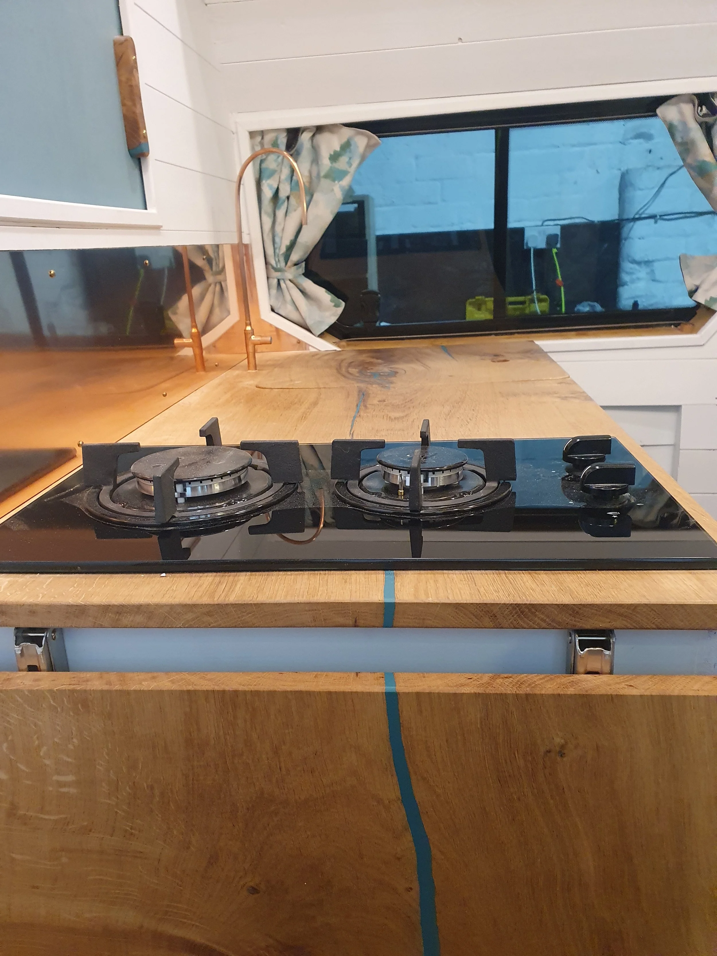 High-roof Vauxhall Vivaro. Semi-fixed bed, Garage space, Heated drying room, Pull out rails, Copper tap, Epoxy poured oak worksurface, Butlers sink, 2 ring hob. Photo 7 of 9.