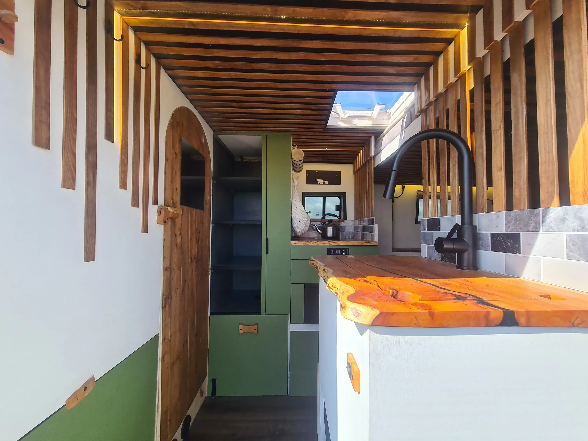 A one-off kitchen with a live-edge worktop, green cupboards, and a wooden door.